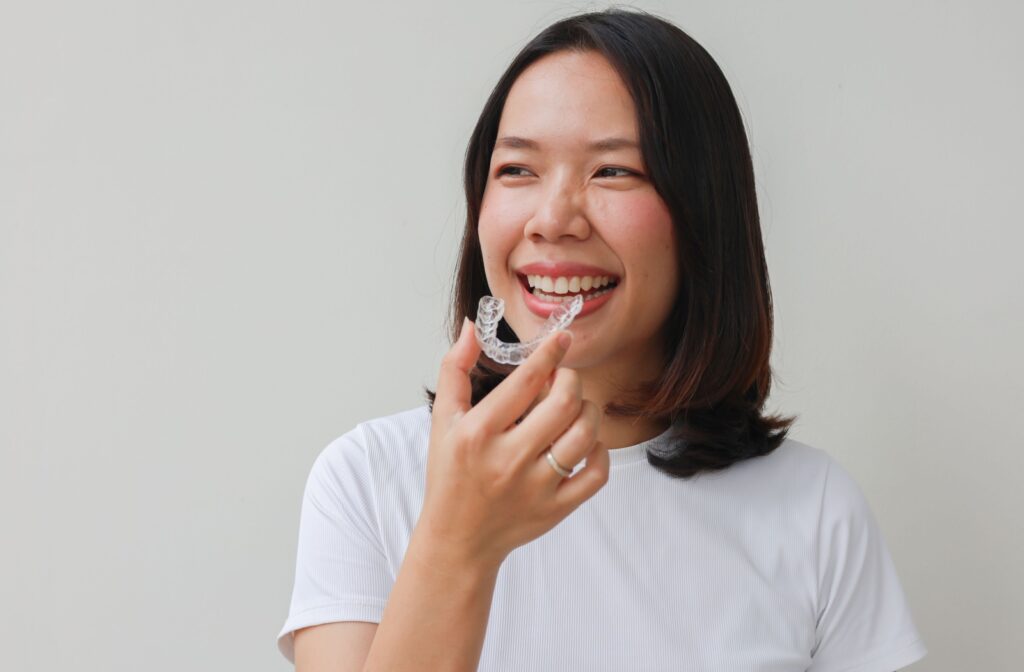 Smiling young asian woman putting in an Invisalign aligner.