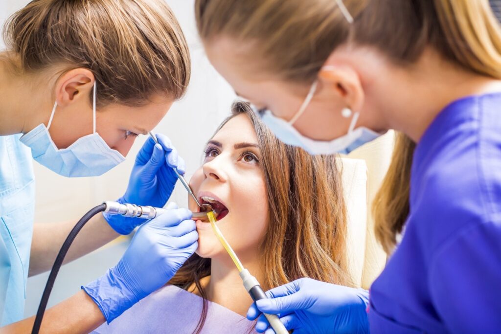 Dental team performing tooth filling procedure on comfortable patient in modern dental office with assistant and hygienist.