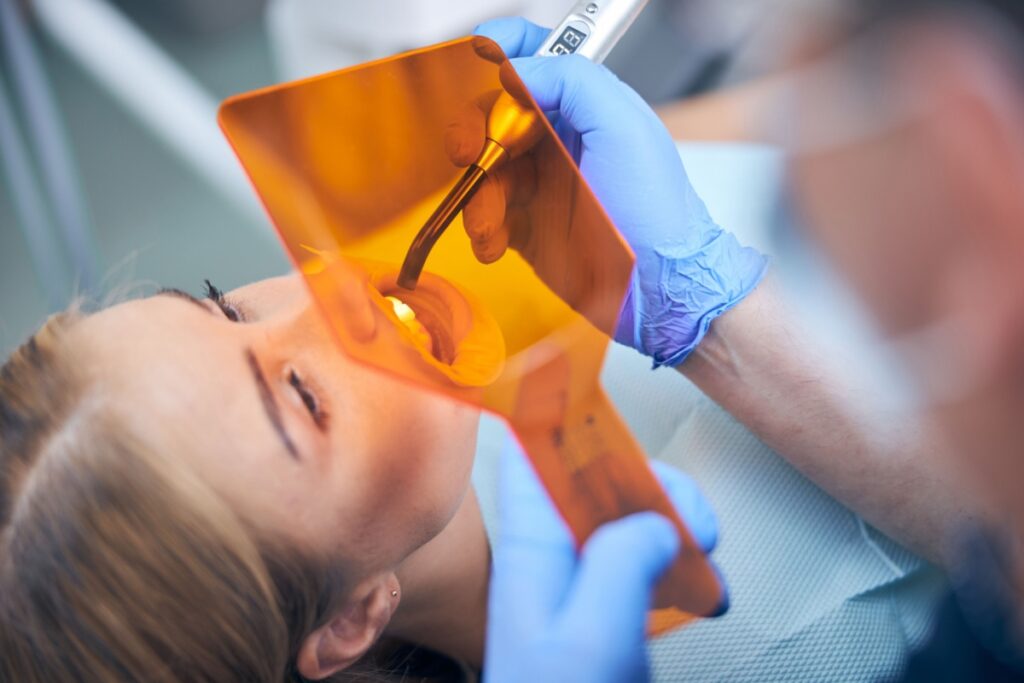 Dentist examining dental X-ray film with orange protective shield to detect cavity and plan tooth filling treatment.