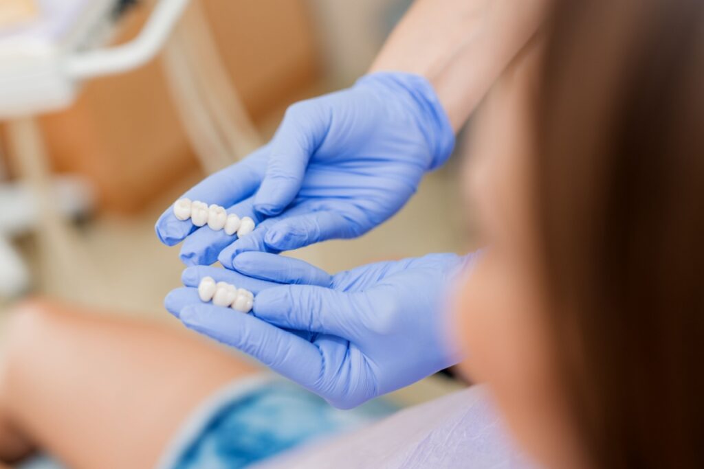Dental professional wearing blue gloves holding dental bridge prosthetic device during patient consultation.